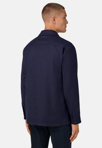 Námořnická modrá košile s límcem, knoflíkovými manžetami a texturovanou tkaninou. Má hladký, čistý vzhled bez viditelných log.