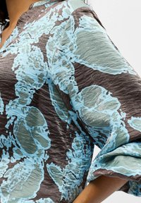 Colorful blouse featuring a floral pattern in light blue and dark brown, with a textured fabric and a relaxed fit.
