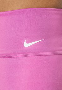 Różowy, elastyczny pas z gładką fakturą, z białym logo Nike po lewej stronie i płaskimi szwami wzdłuż krawędzi.