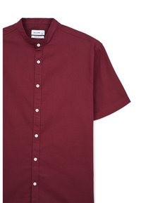 Chemise à manches courtes, coupe régulière, en tissu bordeaux profond. Elle présente un col montant et des boutons blancs le long de la patte de boutonnage devant.