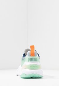 Sneakern har en bakvy med en ljusgrön bas, vit sula, grå detaljer, en orange hälflik och PUMA-logotyp på baksidan.