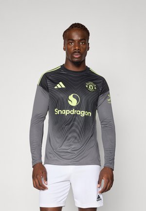 Grijze voetbaltrui met lange mouwen, zwarte geometrische patronen, gele accenten en Adidas-logo. Draag met witte shorts.