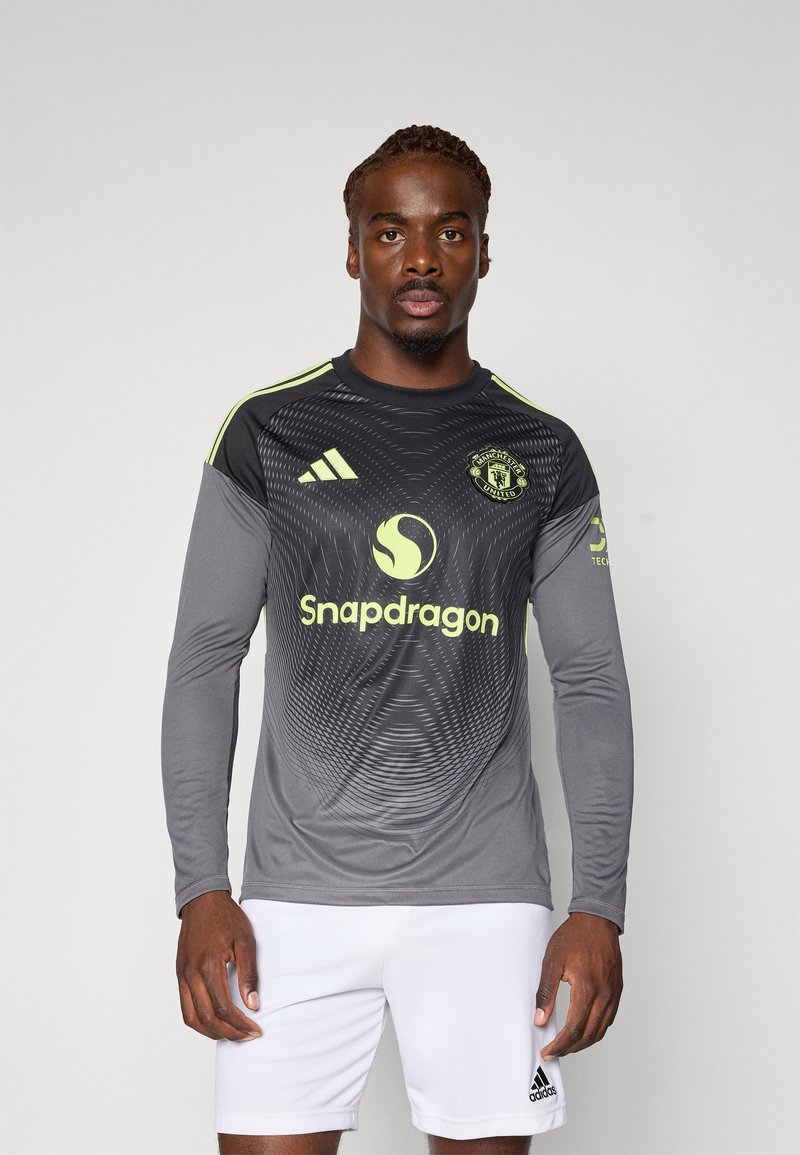 Langärmliges graues Fußballtrikot mit schwarzen geometrischen Mustern, gelben Akzenten und Adidas-Logo. Getragen mit weißen Shorts.