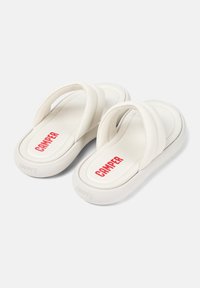 Vita flip-flops med en mjuk, vadderad rem och en tjock sula. Innersulan har "CAMPER" i röd text. Slät textur och minimalistisk design.