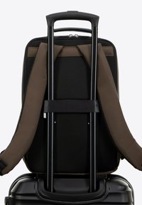 Valigia con scocca rigida nera, manico retrattile nero e spallacci in tessuto marrone. Pannello posteriore in rete per la ventilazione.