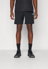 Black athletic shorts with a smooth texture, featuring a light blue Adidas logo. Worn with black socks and shoes, standing on a neutral background.