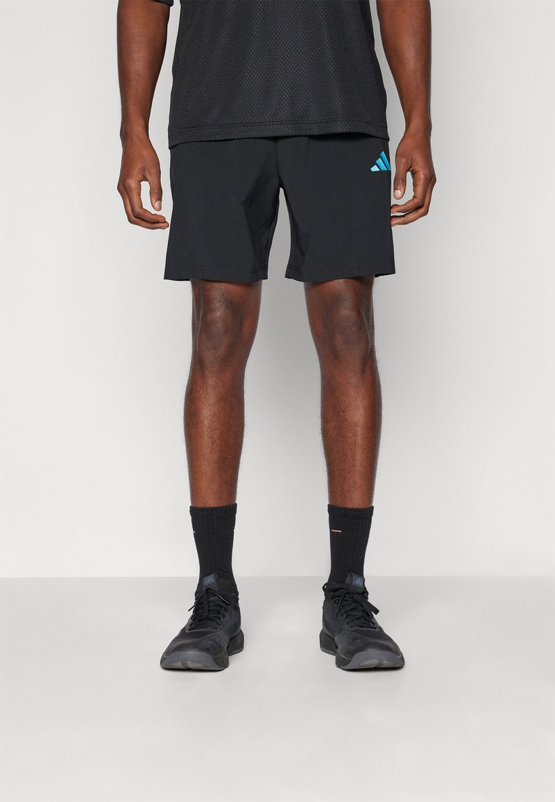 Black athletic shorts with a smooth texture, featuring a light blue Adidas logo. Worn with black socks and shoes, standing on a neutral background.