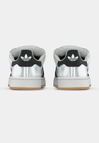 Juodi ir sidabriniai sportbačiai su lygiu viršumi, tekstūruota nugara, putplasčio apykakle ir guminio padais, ant kulno pavaizduotas Adidas logotipas.