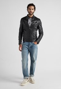 Zwart leren motorjack met gequiltte schouderaccenten, voorritssluiting, twee zijzakken, gedragen over een grijze top en gecombineerd met licht gewassen jeans.