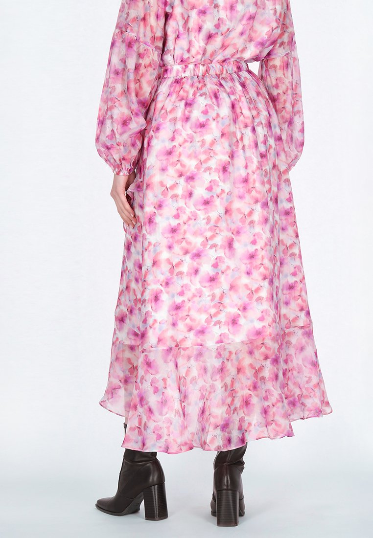 Langes, florales Kleid aus transparentem Stoff mit pinken und weißen Mustern, elastischem Bund, langen puffigen Ärmeln und einem ausgestellten Saum. Getragen mit braunen Absatzstiefeln.
