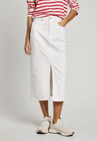 Hvit denim midi-skjørt med spalt foran, høy midje og sidelommer, parret med beige snøresko og en topp med røde striper.