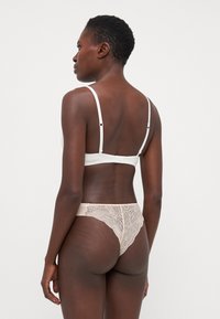 White bra with thin straps and a hook closure, paired with beige lace thong featuring intricate leaf patterns and sheer detailing.