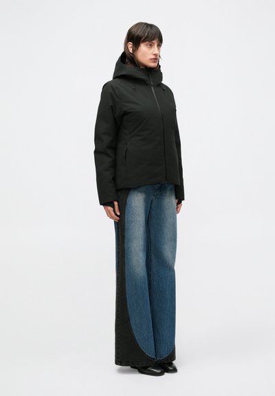 Crna jakna s kapuljačom i patentnim zatvaračem, bočnih džepova; uparena s trapericama širokih nogavica koje imaju tamne i svijetle traper blokove boja.