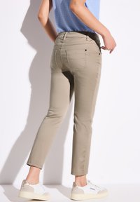 Vihreät slim-fit-housut, joissa on takataskut, ommeltuja yksityiskohtia ja sileä, kevyt materiaali, yhdistettynä valkoisiin lenkkikenkiin.