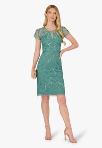Krótka sukienka w kolorze morskim z przezroczystymi, krótkimi rękawami, ozdobiona metalicznymi wzorami z nici i dekoltem z wycięciem. Gładka tkanina o lekkiej fakturze.