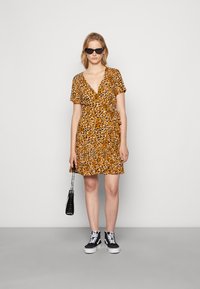 Vestido envolvente de manga curta na cor laranja com estampado animal em preto e castanho. Apresenta uma bainha com franja, combinado com ténis pretos e uma bolsa pequena.