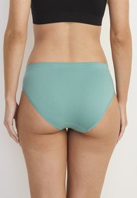 Ljus teal underkläder med en slät textur, medelhög midja och mjuk midjeband. Bakifrån visar de full täckning med sömlösa kanter.