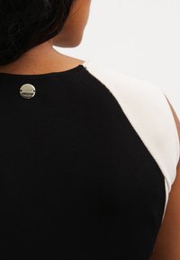 Canottiera a righe bianco e nero in tessuto a coste, con scollatura rotonda e dettaglio di bottone metallico sul retro.