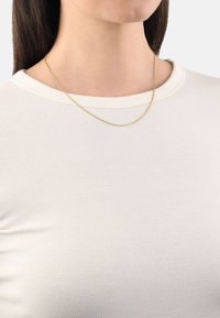 Guldhalsband med en fin, texturerad design, som vilar på en ljusrandig topp med rund halsringning. Enkelt och elegant.