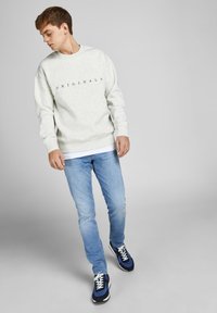 Light gray sweatshirt with "ORIGINALS" text, paired with light blue jeans and navy sneakers. Casual fit with ribbed cuffs and hem.
