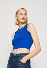 Top corto azul de canalé con escote redondo, diseño sin mangas y silueta ajustada. Combinado con jeans de mezclilla oscura.