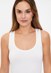 White scoop-neck tank top made of smooth cotton fabric. Features narrow straps and a fitted silhouette, ideal for layering or casual wear.