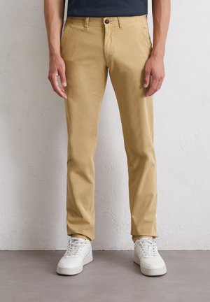 Khaki cotton pants with a straight-leg design, featuring front pockets, a zip fly, and a single button closure, paired with white sneakers.