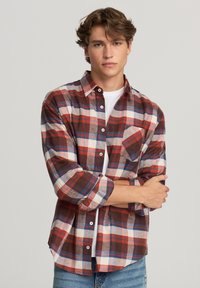 Camicia di flanella a scacchi rossa, blu navy e bianca. Presenta una tasca sul petto, colletto con bottoni e maniche lunghe con risvolti.