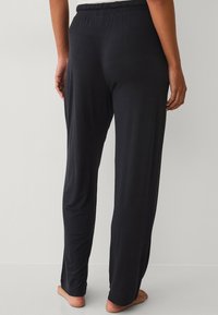 Zwarte, lichtgewicht pyjamabroek met een elastische tailleband. Rechte pijpen en een gladde textuur. Geen zichtbare zakken of versieringen.