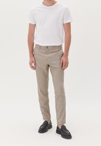Lichtbeige broek met een subtiele ruitpatroon, slim fit, gladde textuur, voortzakken en een enkele knoopsluiting, gecombineerd met een wit shirt.