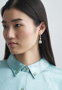 Silverhängande örhängen med blommiga detaljer, prydda med klara stenar, ihop med en mintgrön skjorta med krage i mjukt tyg.