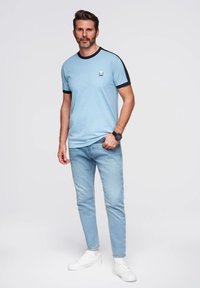 Světle modré tričko s krátkým rukávem a černým lemem, zdobené malým logem, spojené se světle modrými úzkými džíny a bílými teniskami.