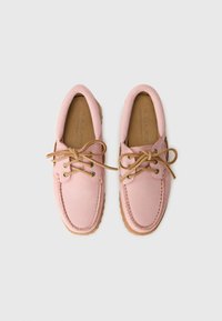 Pair of pink suede boat shoes with tan laces and stitched details on a light gray background.