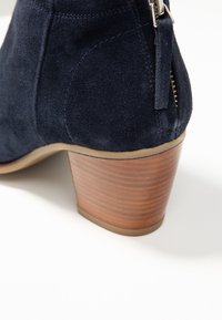 Stivaletto alla caviglia in camoscio blu navy con tacco in legno impilato, chiusura con zip e cuciture dettagliate lungo i lati.