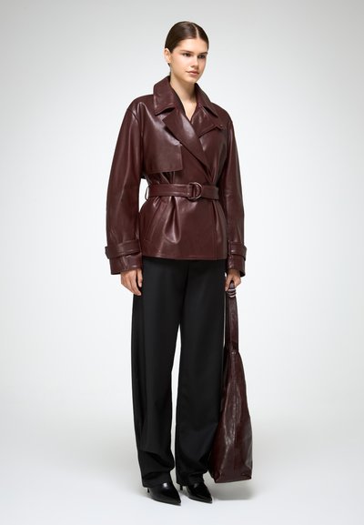 Bordeaux leren trenchcoat met riem en een oversized kraag, gecombineerd met zwarte wijde broek en een bijpassende leren tote bag. Soepele textuur.