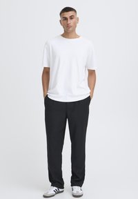 T-shirt blanc à manches courtes associé à un pantalon noir ample et des baskets blanches, sur un fond neutre.