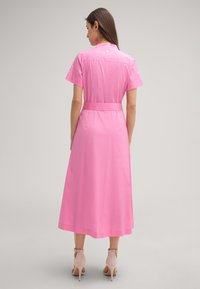 Rosa Midikleid mit kurzen Ärmeln, tailliertem Bund und Kragen; glatte Textur mit einem schlichten Design und einem Knopfdetail auf der Rückseite.