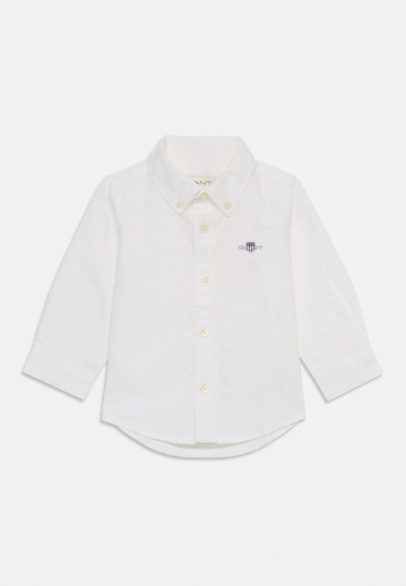 Chemise blanche à manches longues avec boutons, col boutonné et petit blason brodé sur la poitrine gauche.