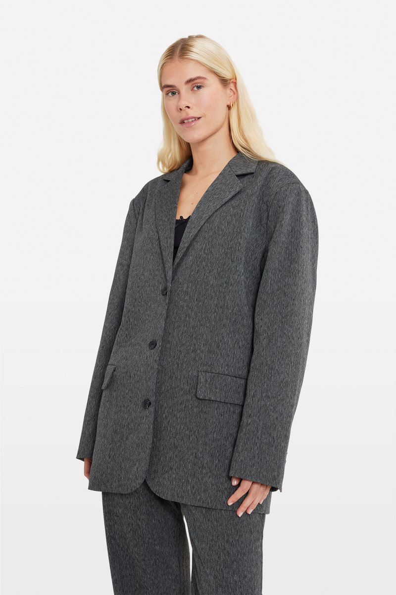 Blazer en mélange de laine gris avec un revers cranté, deux poches avant et fermeture à bouton. Tissu texturé avec un subtil motif en chevrons.