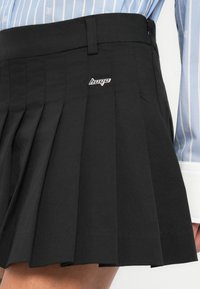 Μαύρη φούστα με πιέτες από λείο ύφασμα, με φερμουάρ στο πλάι και ασημένια λεπτομέρεια με λογότυπο στη μέση.