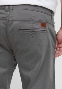 Grau Hosen mit einer glatten Textur, ausgestattet mit einer Gesäßtasche mit Knopf, einem kleinen Leder-Logo-Patch und einem modernen Schnitt.