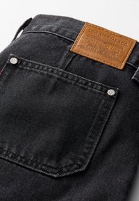 Poche arrière d'un jean Levi's noir avec une étiquette en cuir marron Levi Strauss & Co. et des rivets argentés aux coins de la poche.