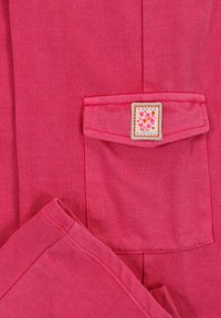 Roze katoenen kledingstuk met een zak en een bloemenlabel. Gladde textuur, eenvoudig ontwerp en zichtbare stiksels.