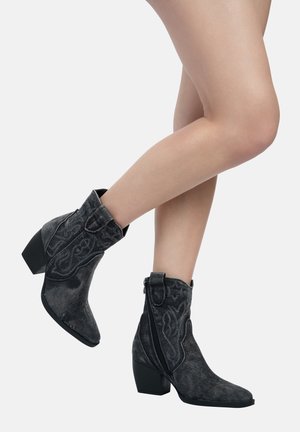 Stivaletti neri in suede con punta appuntita, tacco basso a blocco e motivi decorativi di cucitura. Presentano una cerniera laterale per la chiusura.