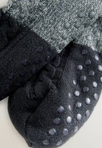 Calcetines de punto en negro y gris con superficie texturizada y puntos de agarre de goma en las suelas. Presentan un diseño de punto trenzado y un acabado suave.
