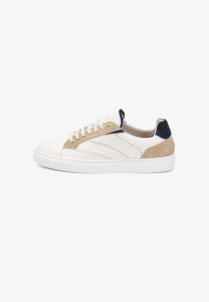 Witte lage sneaker met beige suède accenten, navy hielstuk, witte veters en geperforeerde details aan de zijkant op een witte zool.