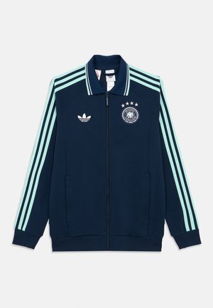 Tumesinine täieliku lukuga jakk, millel on hele sinised kolmekordsed triibud varrukatel, Adidas logo ja nelja tärniga Saksa jalgpallimärk rinnal.
