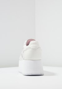 Vita plattformssneaker med slät lädermaterial, rund tå och texturerad gummisula. Har präglad branding på hälen.