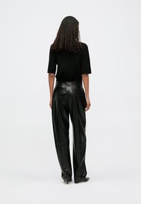 Top de malha pregueada preta com mangas curtas combinado com calças largas de couro preto de cintura alta. Textura suave, design minimalista, dois bolsos traseiros.
