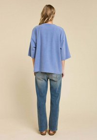 Un haut oversized bleu clair à manches courtes, associé à un jean droit délavé. Le tissu semble doux, avec une coupe décontractée et un minimum de détails.